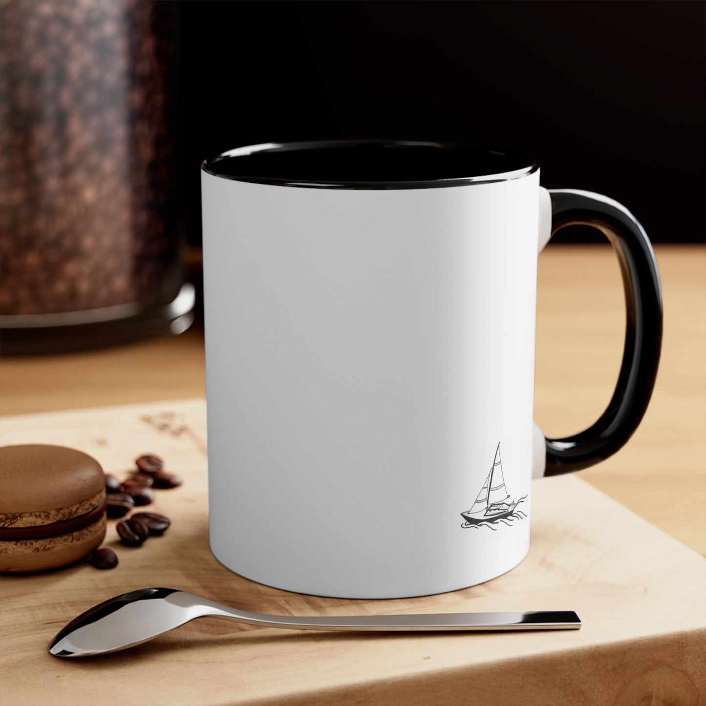White Coffee Mug with Black Handle and sailboat on front, sitting on table