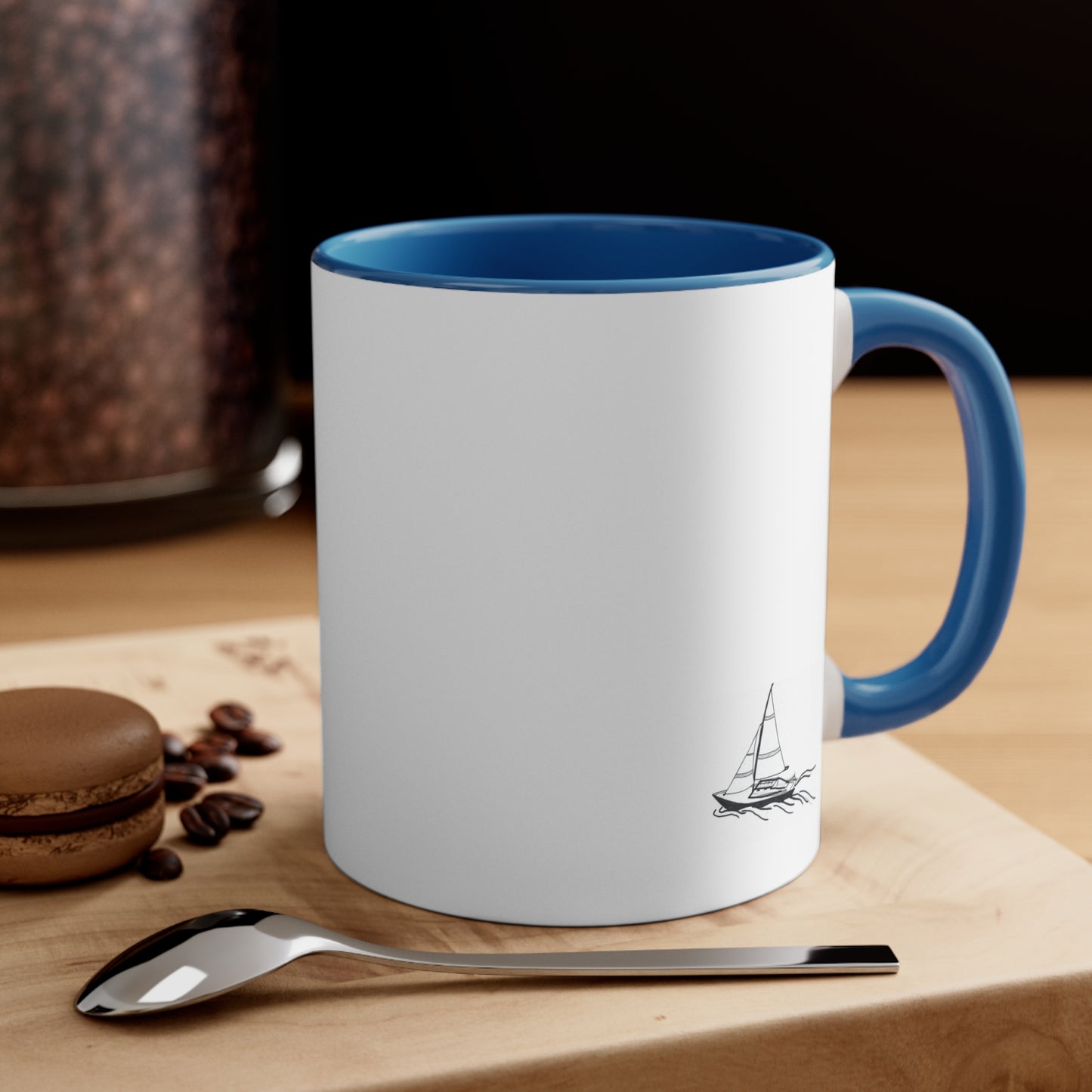 White Coffee Mug with Blue Handle and sailboat on front, sitting on table