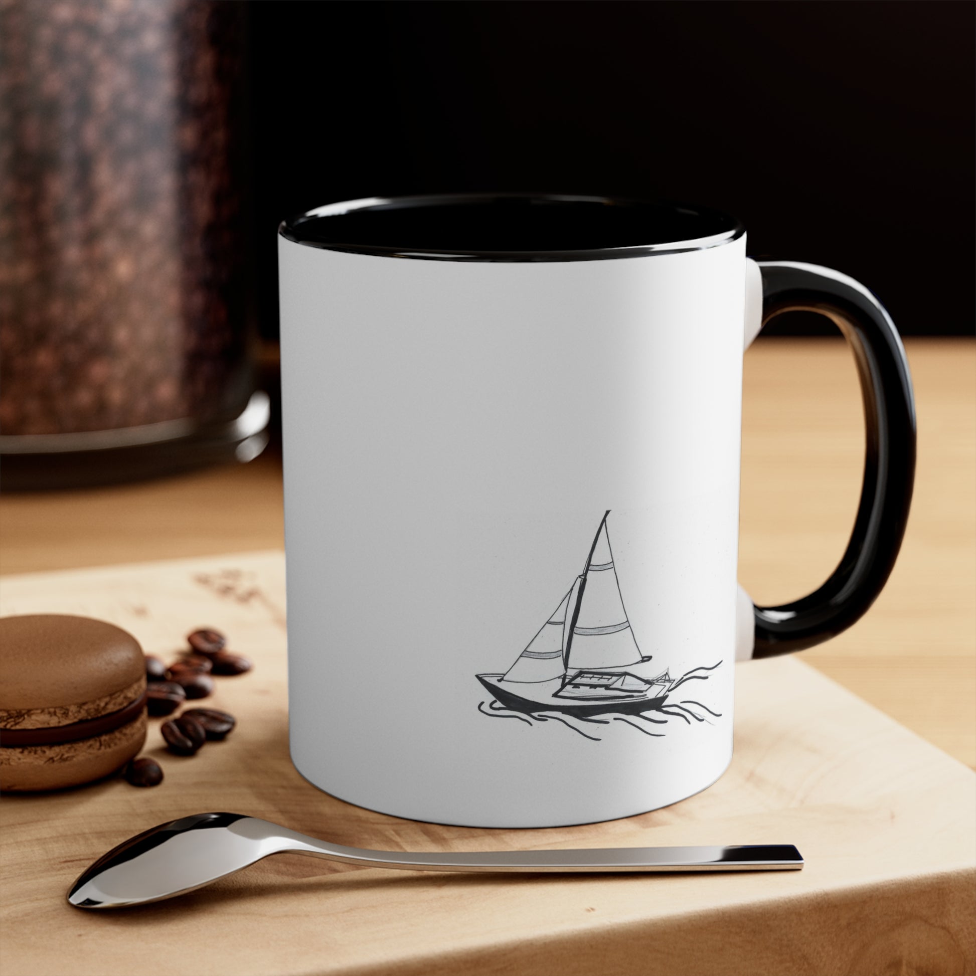 White and Black Coffee Mug with Sailboat on back sitting on a table